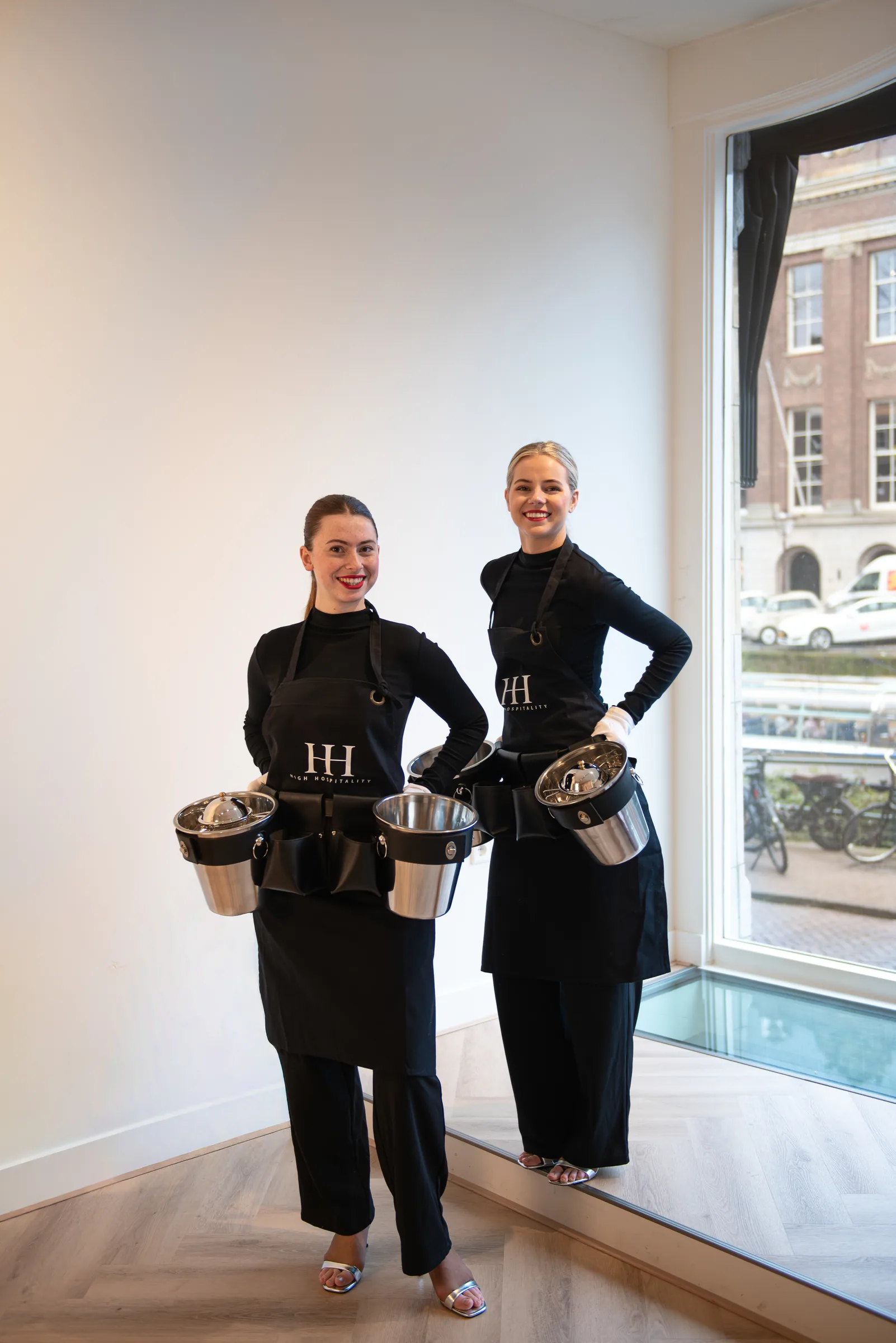 Twee High Hospitality-hostesses in zwarte servicekleding met serveeruitrusting