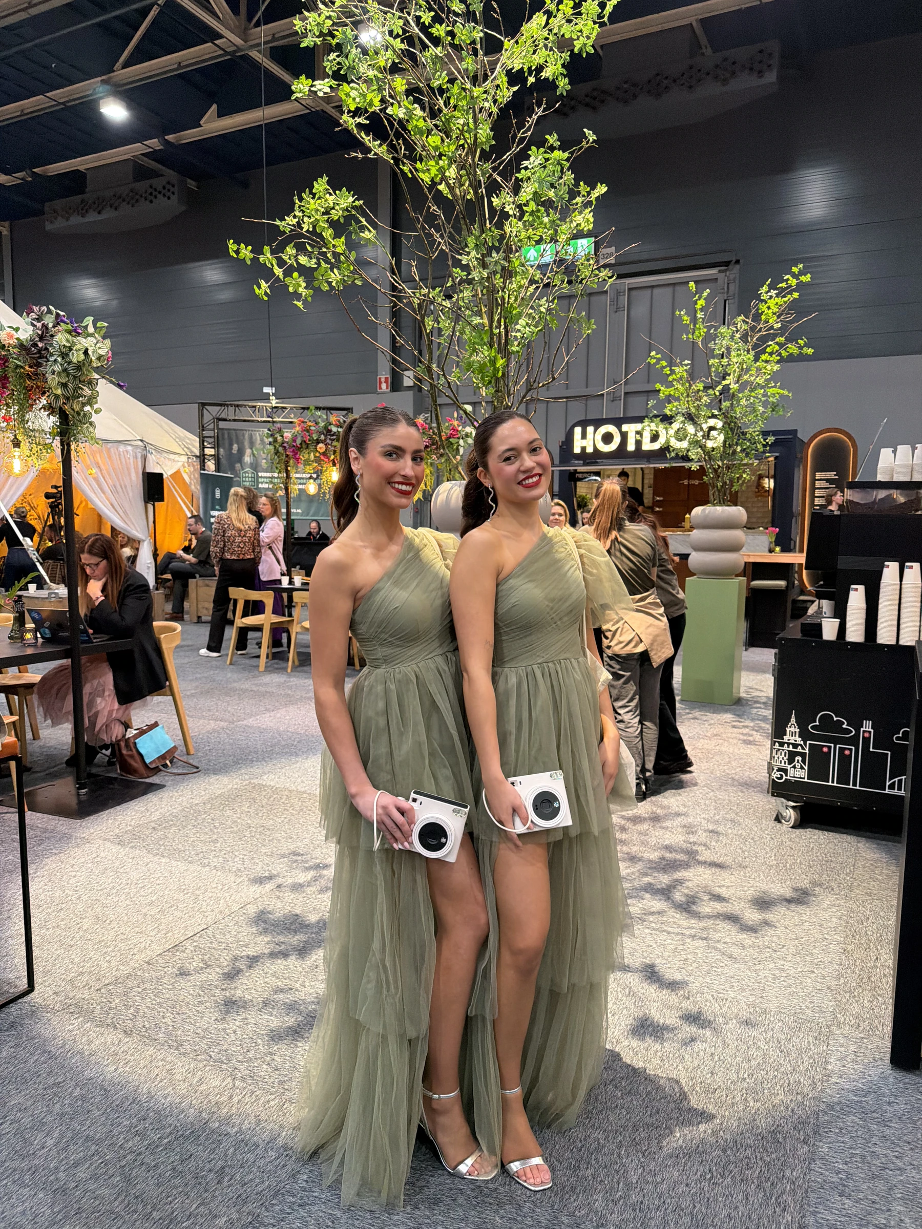 Two Polaroid Girls in green dresses holding instant cameras at an event