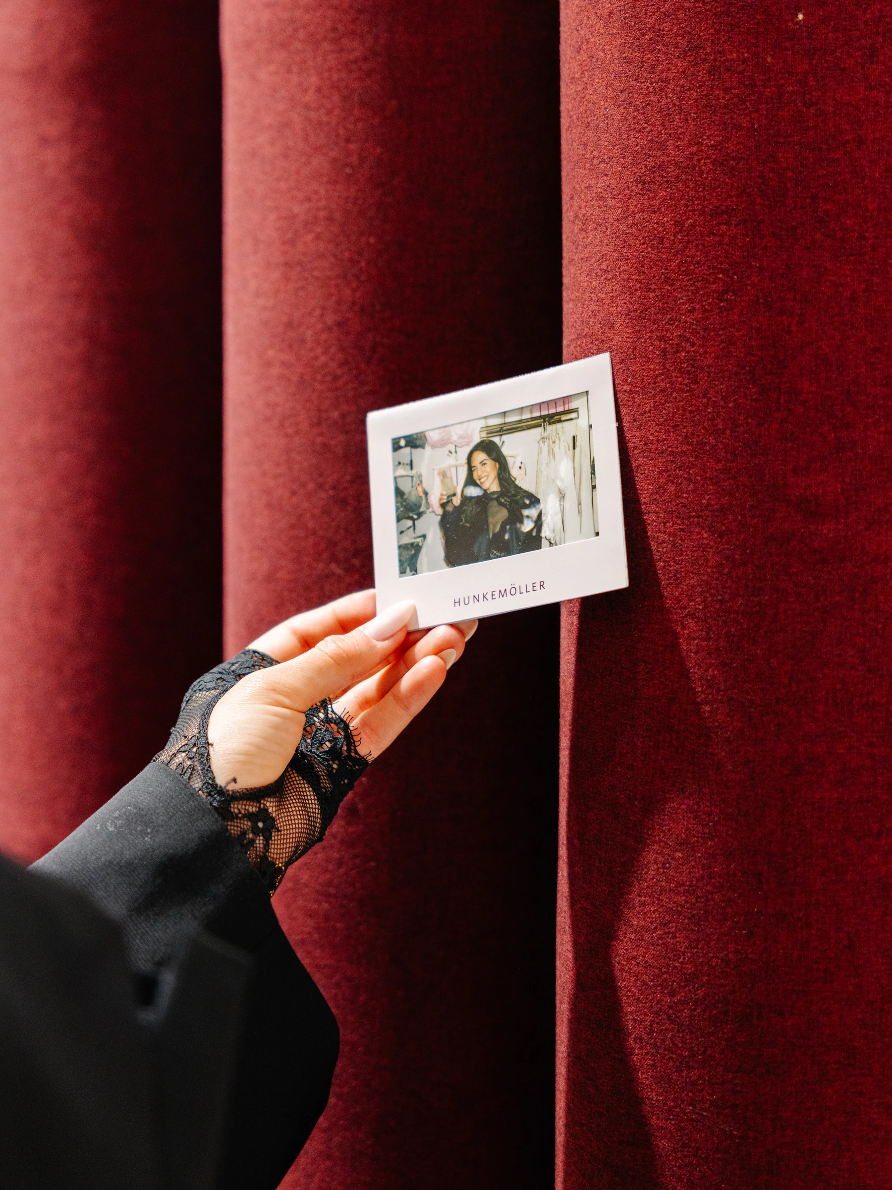 A hand holding a personalised Hunkemöller Polaroid in front of a red curtain